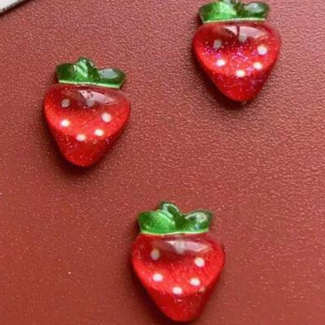 Three red strawberry-shaped charms on a brown background