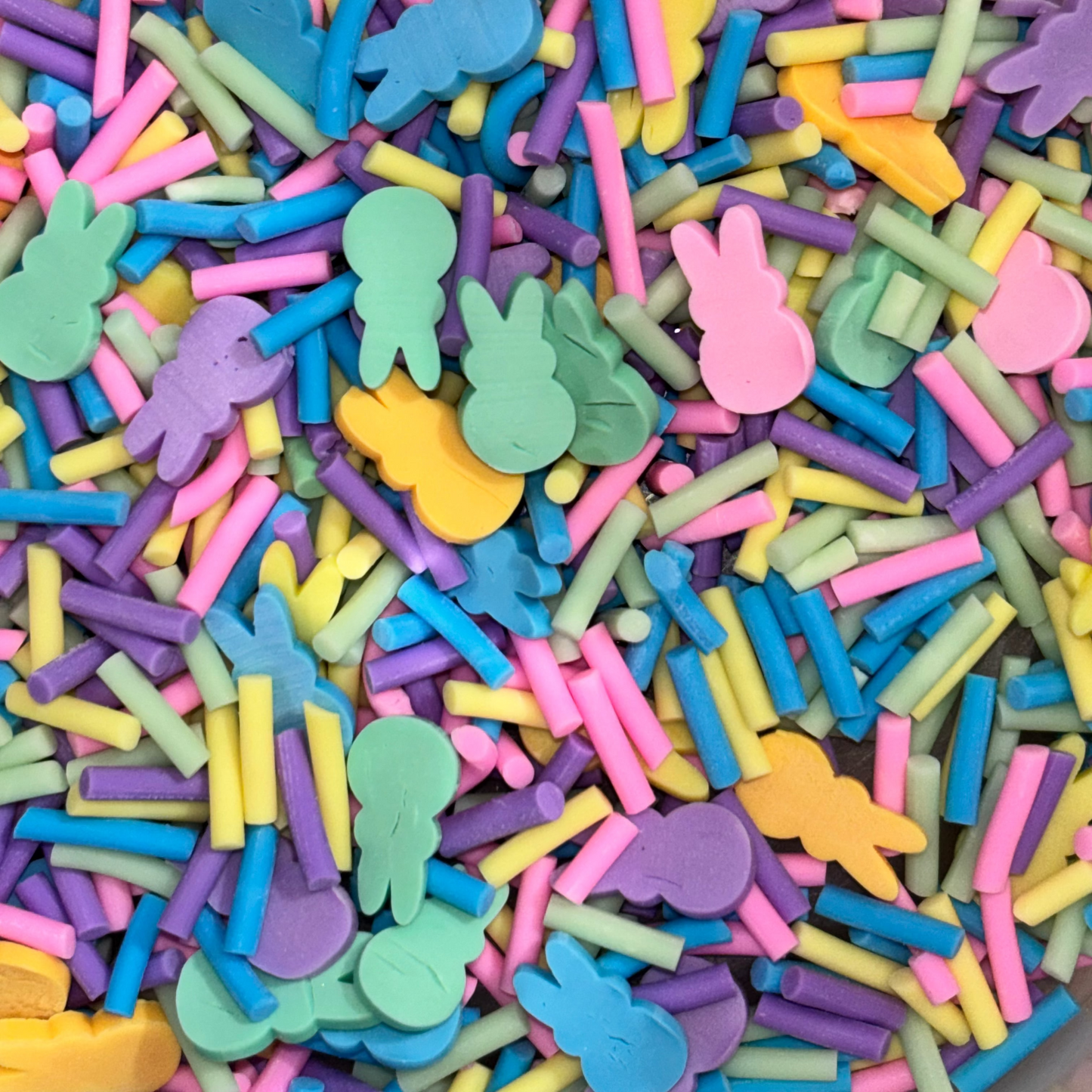 A close-up view of a pile of colorful Easter-themed sprinkles, including pastel pink bunnies, yellow, blue, green, purple and yellow clay sprinkles.