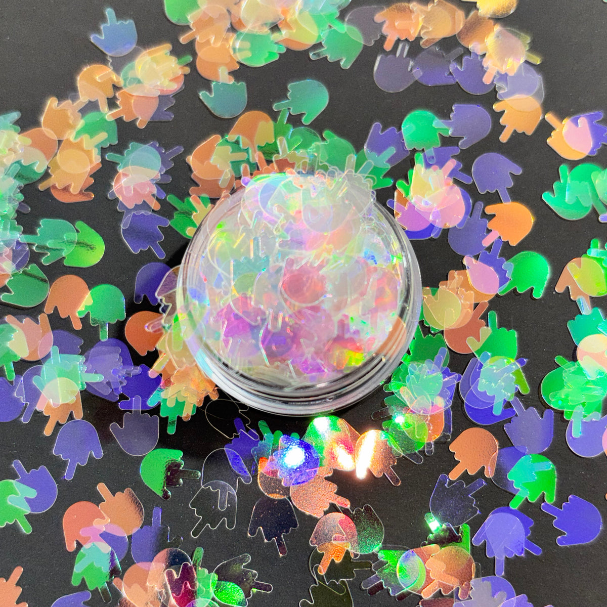 Holographic ghost-shaped confetti scattered on a black surface with a container of confetti in the center.