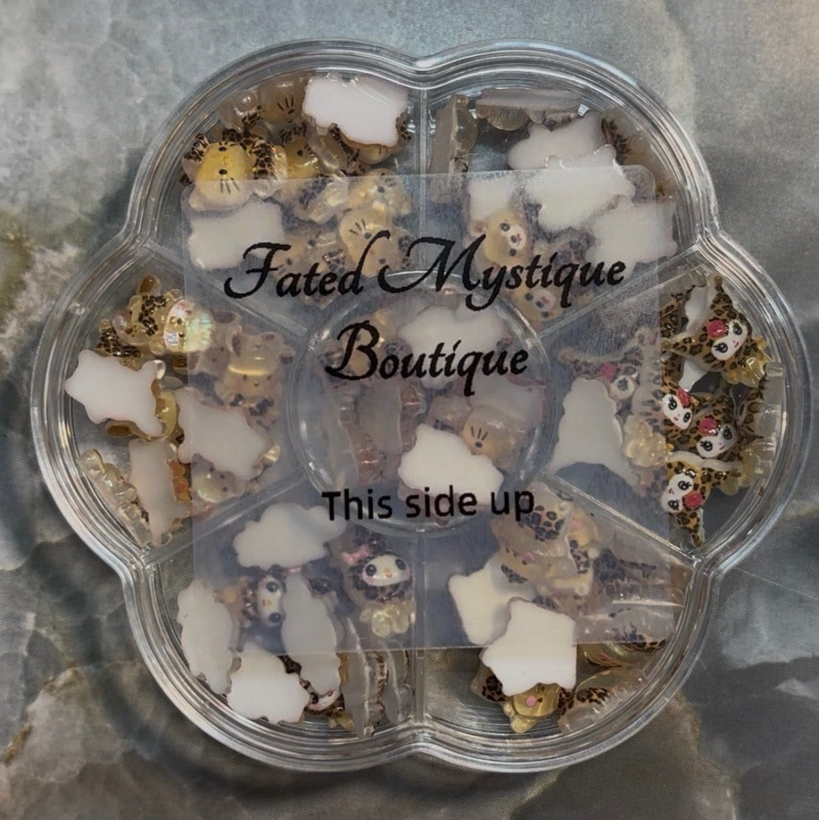 Transparent container with decorative items labeled 'Fated Mystique Boutique' on a gray surface.