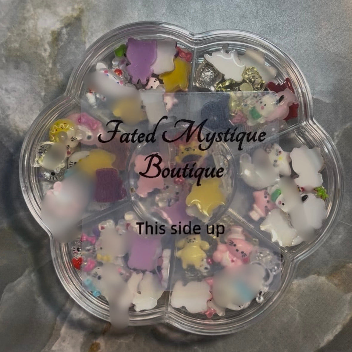 Clear plastic container with colorful small figurines on a gray surface, branded 'Fated Mystique Boutique'.