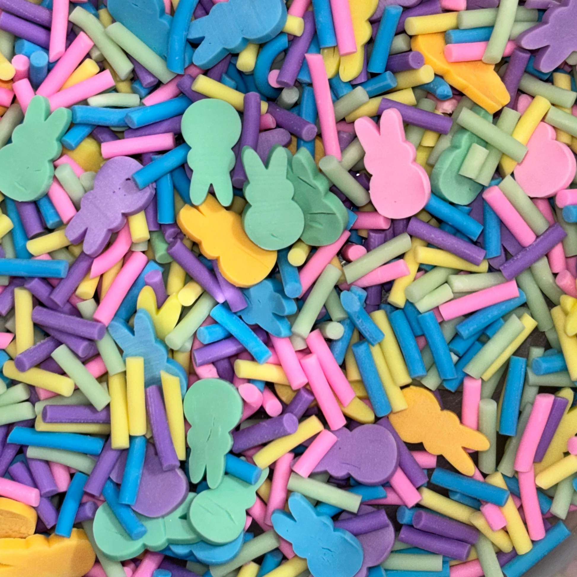 A close-up view of a pile of colorful Easter-themed sprinkles, including pastel pink bunnies, yellow, blue, green, purple and yellow clay sprinkles.