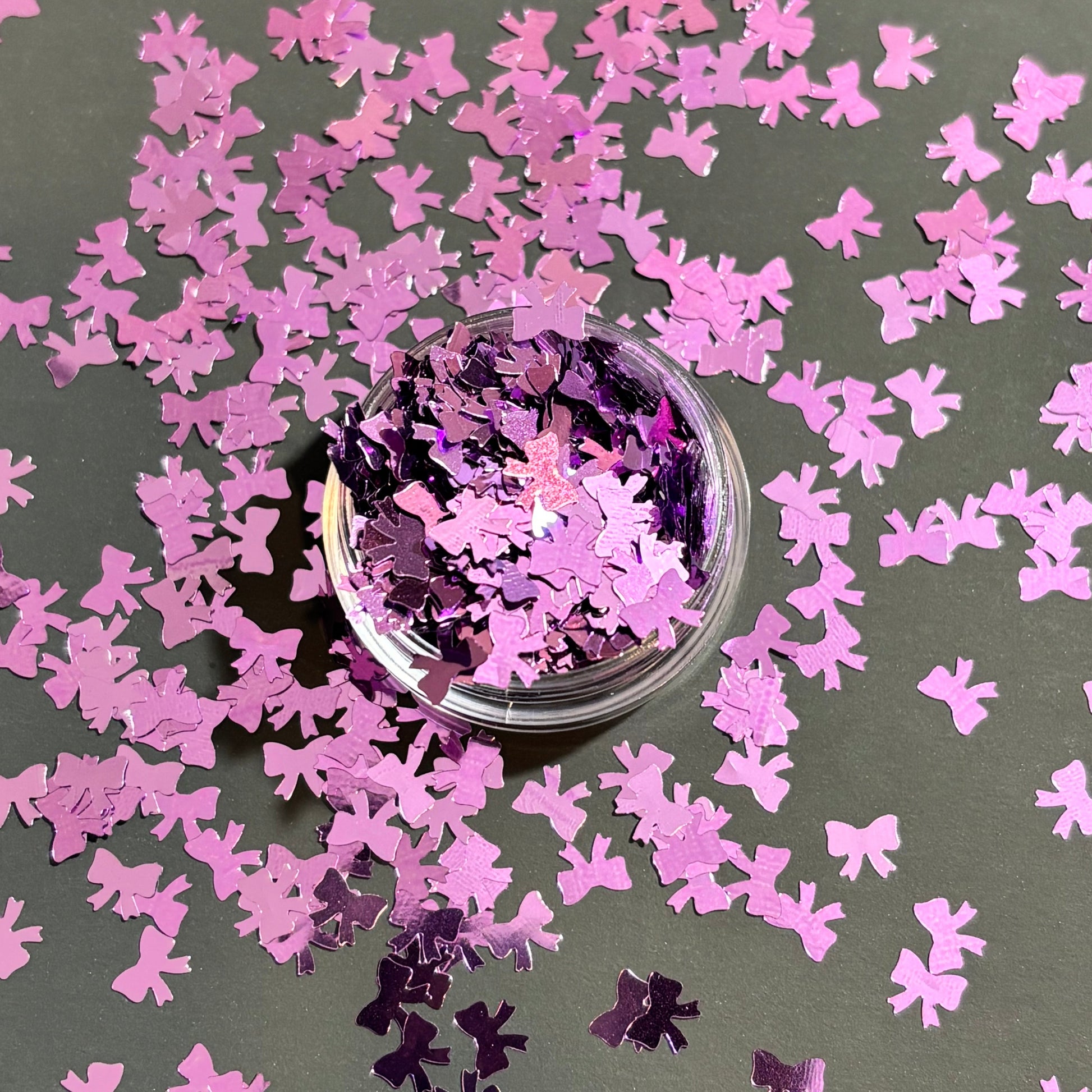 purple bow-shaped confetti scattered on a dark surface with a small container of confetti.