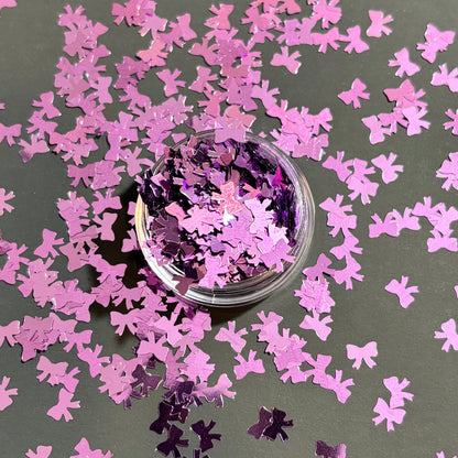 purple bow-shaped confetti scattered on a dark surface with a small container of confetti.