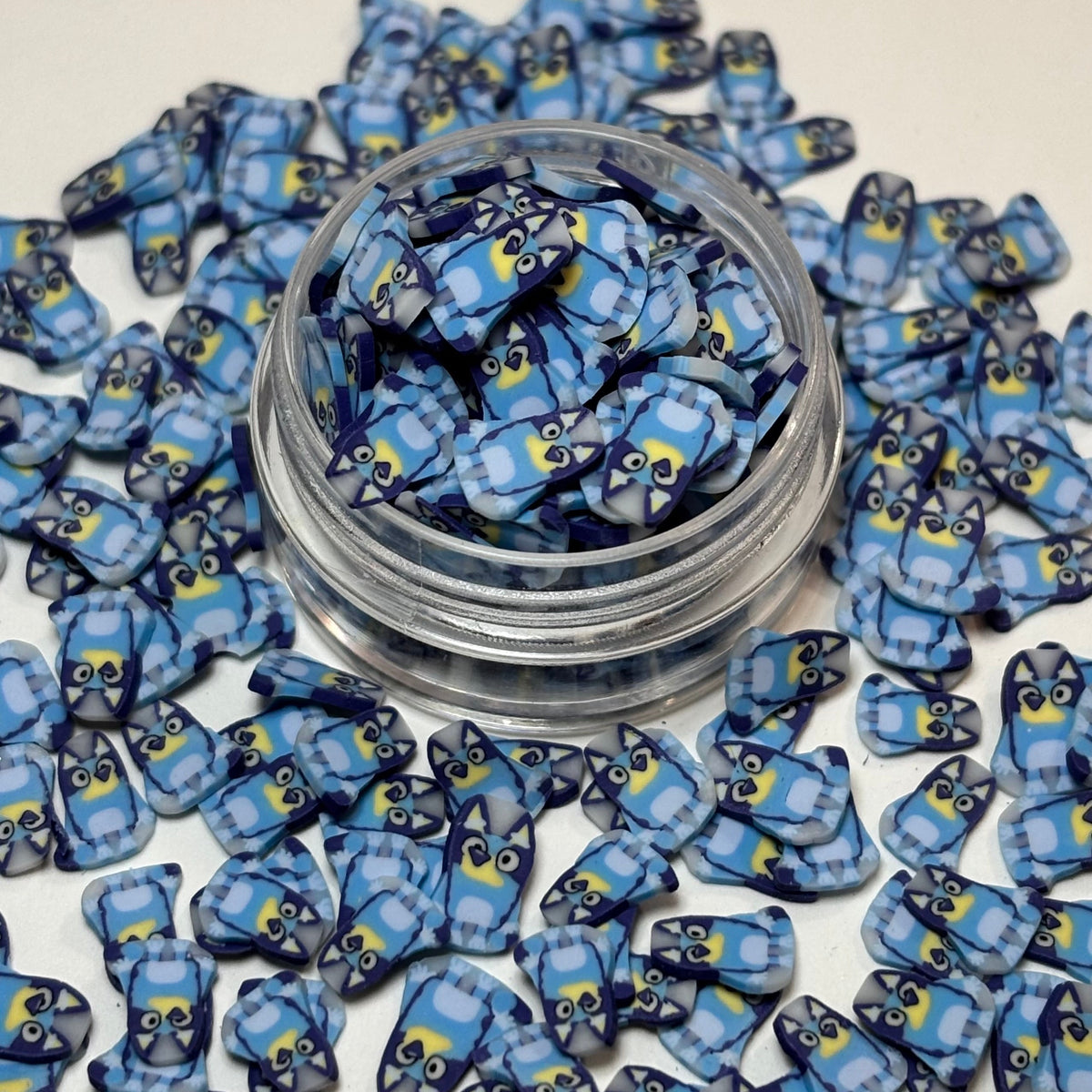 Blue and yellow owl-shaped craft embellishments scattered around a small clear plastic jar on a white background.
