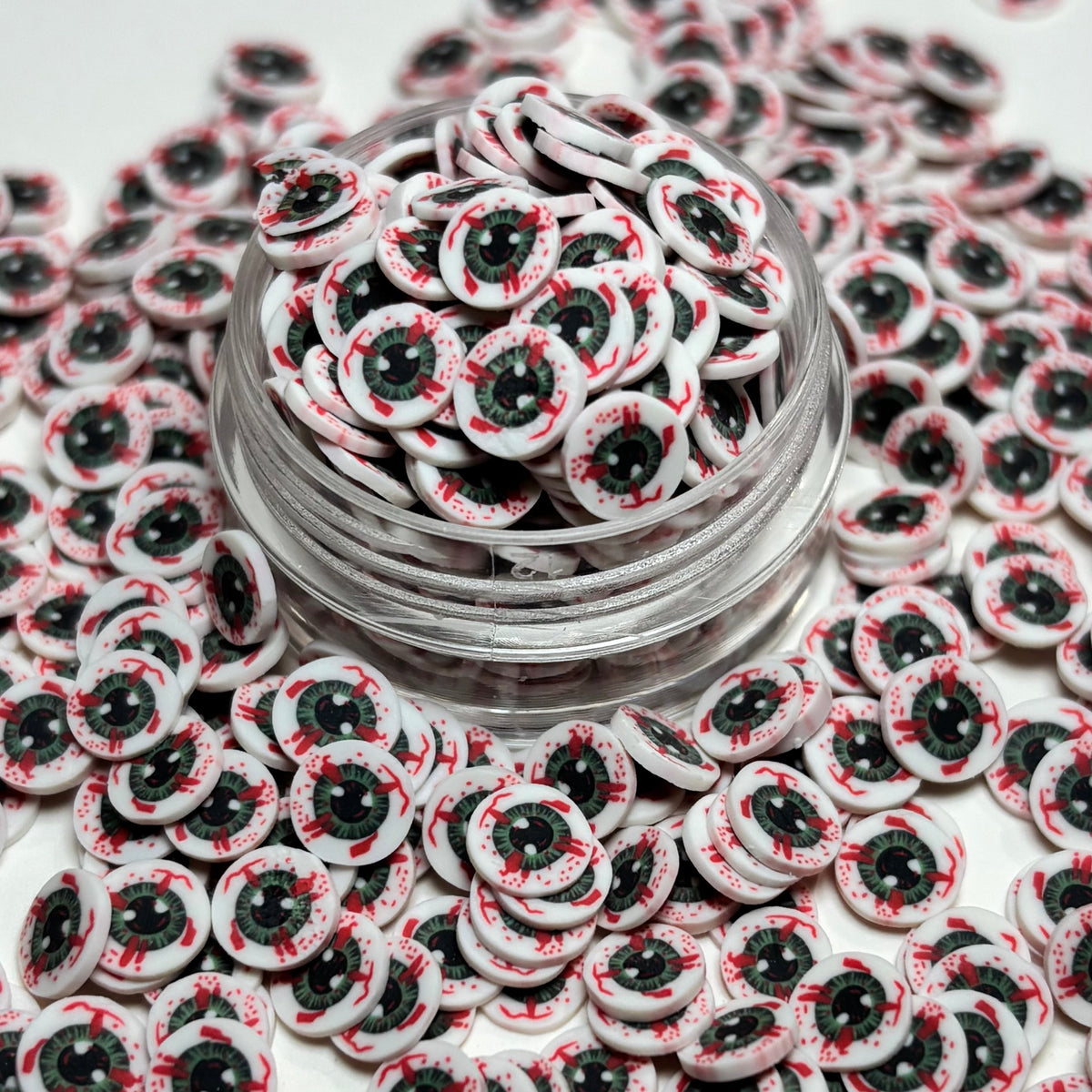 Small round white goggle-shaped embellishments with black and red details, shown piled in a clear jar with more of the same scattered around on a white background.