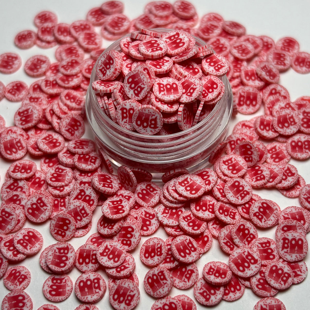 Red and white sugar-coated round nail art stickers with '888' printed on them, shown in a clear jar with more scattered around on a white background.