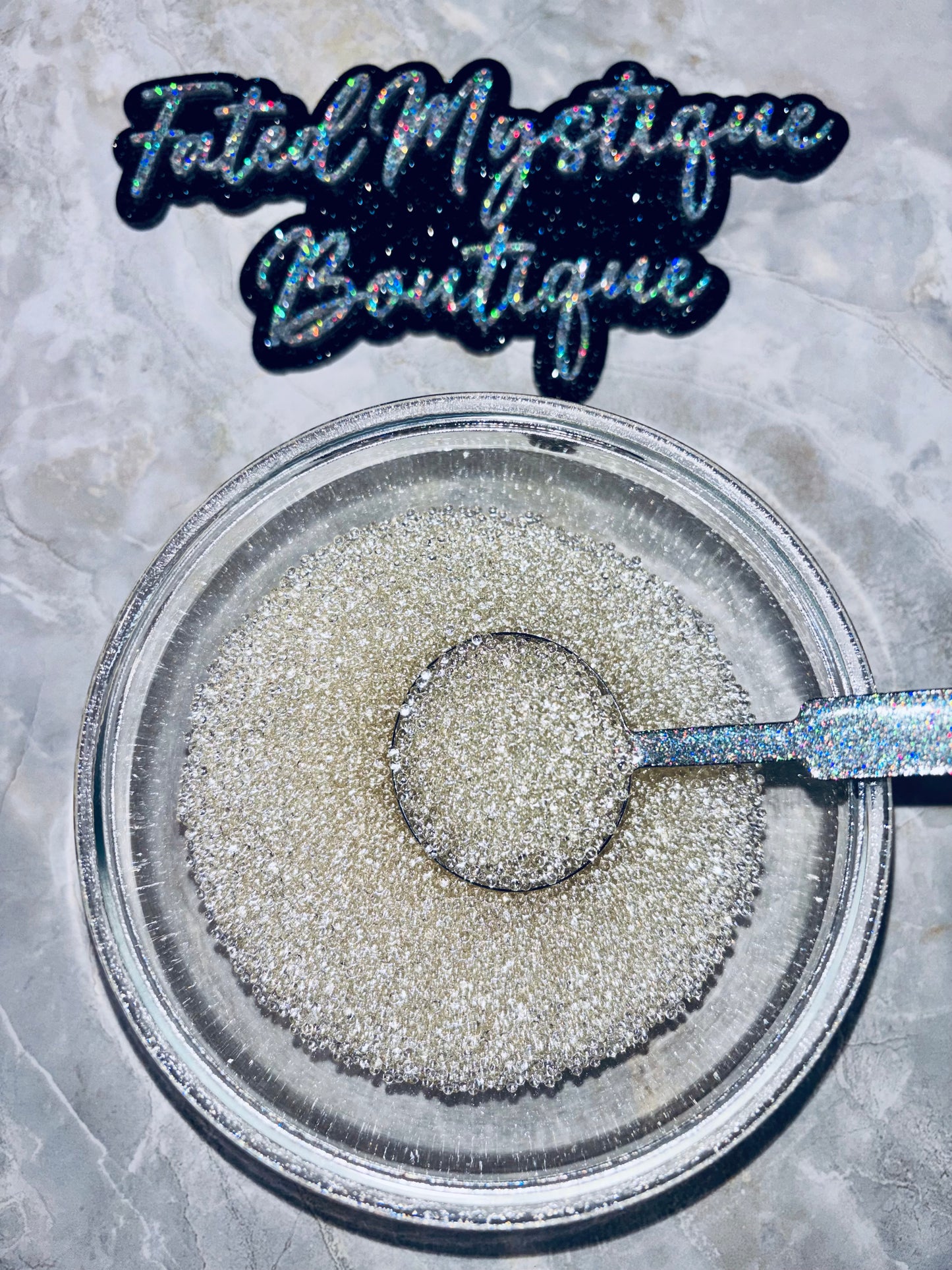 Silver glitter in a clear container with a spoon, branded 'Fated Mystique Boutique'.