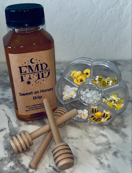 Bottle of Honey drip with wooden dipper and bee charms on a marble surface
